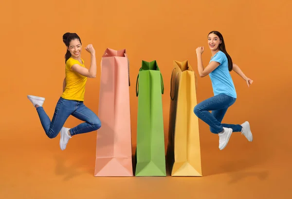 黑色星期五 季节性销售 购物概念 快乐而又多文化的年轻女士穿着时髦的休闲装在巨大的购物袋旁边跳过橙色工作室的背景 抄袭空间 拼凑在一起 — 图库照片