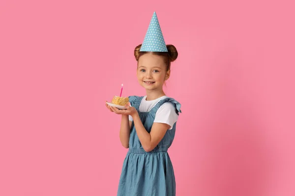 誕生日パーティーを持つハッピーかわいい女の子 キャンドル付きケーキを保持し カメラを見て ピンクのスタジオの背景に楽しいを持っている紙の帽子で陽気な十代の女性の子供 スペースをコピー — ストック写真