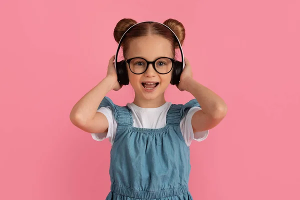 可爱快乐的小女孩头戴无线耳机 快乐的少女听音乐 快乐快乐快乐的小孩一边站在粉色背景上一边欣赏心爱的歌曲 — 图库照片