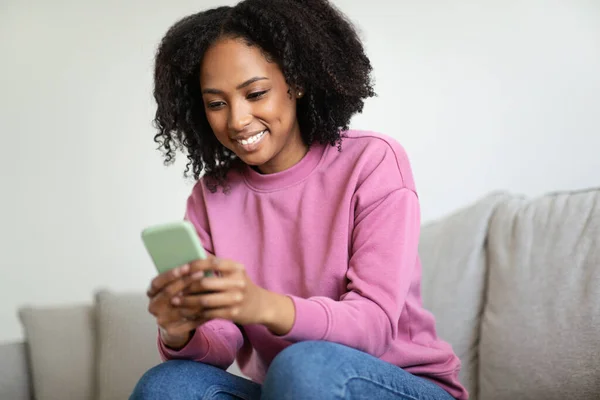 Feliz Mulher Negra Milenar Digitando Smartphone Mensagem Sentado Sofá Interior — Fotografia de Stock