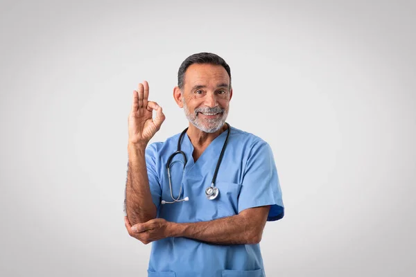Χαίρομαι Καυκάσιος Ώριμος Γιατρός Μπλε Στολή Δείχνουν Σημάδι Χέρι Απομονώνονται — Φωτογραφία Αρχείου