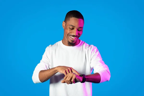 Szczęśliwy Przystojny Młody Czarny Mężczyzna Neonowym Świetle Patrząc Nowoczesny Smartwatch — Zdjęcie stockowe