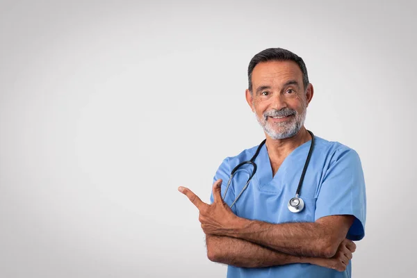 Cirurgião Médico Sênior Caucasiano Positivo Uniforme Azul Apontando Dedo Espaço — Fotografia de Stock