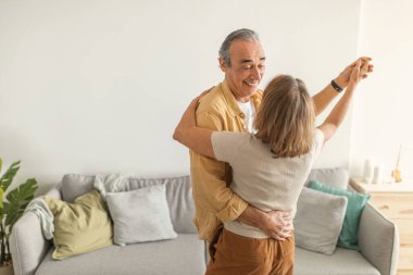 Romantik kıdemli eşler oturma odasında birlikte dans ediyorlar, karı koca el ele tutuşuyorlar ve birbirlerine bakıyorlar, birbirleri ile evde vakit geçiriyorlar.