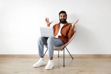 Çevrimiçi Şans. İyi ki Arap adam dizüstü bilgisayarla koltukta oturuyor ve sevinçle el kaldırıyor, harika haberler alıyor ve beyaz arka planda başarıyı kutluyor. Vay be internet teklifi