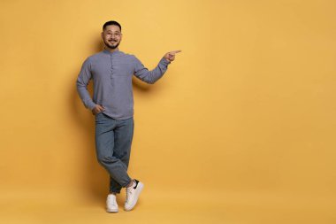 Şuna bak. Elle Boşluğu Kopyalayan Mutlu Asyalı Adam, Sarı Arkaplan 'da Tam Uzunluk' ta dururken Reklam İçin Boş Yer Gösteren Gülümseyen Milenyum Adamı