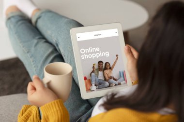 Ekranda internet mağazası olan tablet kullanan, evde kahve içen, web sitesi ya da mobil uygulamanın keyfini çıkaran bir kadın. Alışveriş, moda alışverişi.