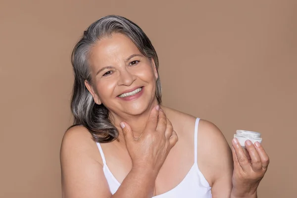 快乐的欧洲裔老妇人的画像 灰白的头发在面部皮肤上涂上奶油 在米色工作室背景上被隔离 美容护理 抗衰老护理治疗的化妆品 — 图库照片