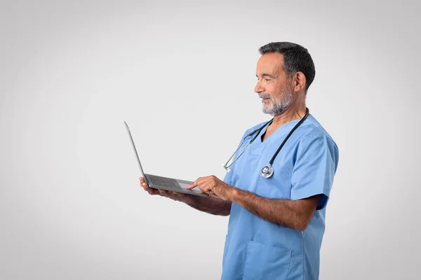Glad Caucasian Mature Man Doctor Uniform Typing Laptop Isolated Gray — Stock Photo, Image