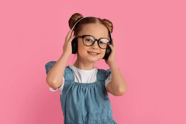 快乐的小女孩戴着无线耳机 听着音乐 可爱的十几岁以下的小女孩欣赏着最喜爱的歌曲 一边站在粉色背景上一边享受着欢乐 一边享受着复制空间 — 图库照片