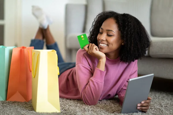 幸せな千年の黒人女性は タブレット クレジットカードを使用したパッケージで床に横たわっており 部屋のインテリアでオンラインショッピングを楽しんでいます 広告やオファー 自宅でガジェットで注文 — ストック写真