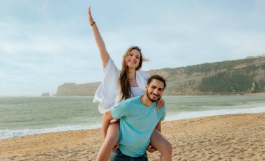 Bin yıllık gülümseyen Arap adam avrupalı kadını sırtında tutuyor, eğleniyor, aşkın tadını çıkarıyor, haftasonu sahilde özgürlüğün tadını çıkarıyor. Tatiller, yürüyüşler, yazın ilişkiler.