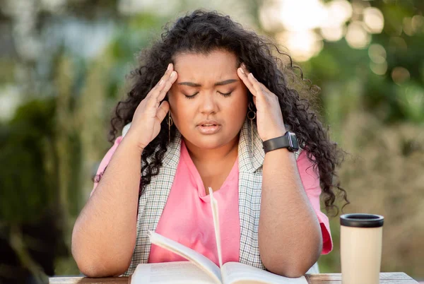 Headache And Educational Stress. Unhappy Student Lady Suffering From Migraine While Learning And Reading Books Sitting Outdoors. Learner Having Painful Head Ache Preparing For College Exams