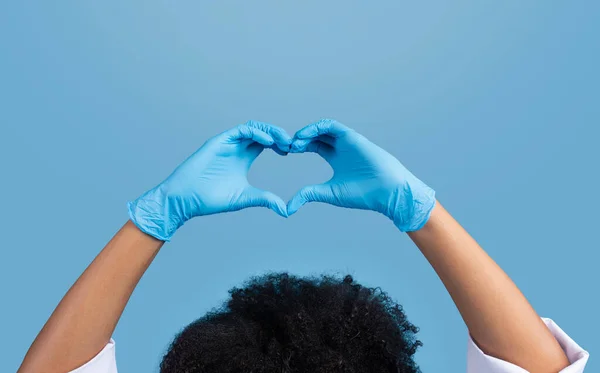 年轻的非洲裔美国卷曲女医生 身穿白衣 戴着防护手套 用手制作心征 与蓝色背景隔离 工作室隔离 爱的姿态 医疗服务 医疗保健 — 图库照片