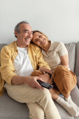 Mutlu yaşlı çift sarılıyor, kanepede oturuyor ve birlikte boş zamanın tadını çıkarıyor, televizyon izliyor, uzaktan kumandaya odaklanıyor. Evde dinlen, aşk ve ilişkiler.