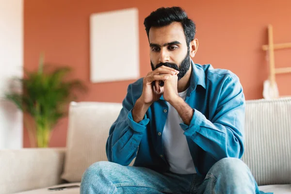严重的问题和思考 沮丧的印度人在想他的问题和烦恼 坐在沙发上在家 带着空虚的表情远眺 男性抑郁症状 — 图库照片