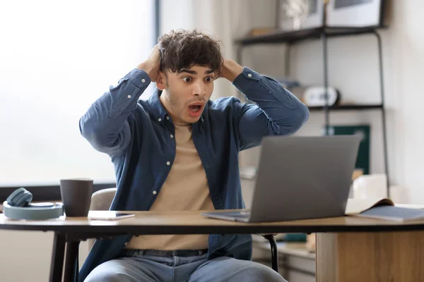 Oops, Problem At Workplace. Shocked Emotional Hispanic Businessman Looking At Laptop Computer Having Issue Working Online Sitting In Modern Office Interior. Internet Connection Error Concept