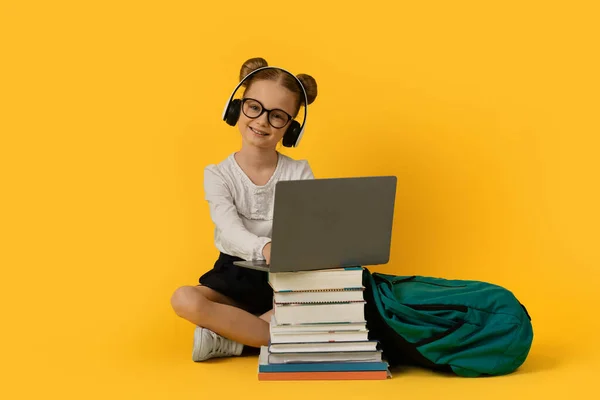 电子学习概念 在黄色工作室背景下使用笔记本电脑 戴着无线耳机 在电脑键盘上打字的可爱小女孩的画像 复制空间 — 图库照片