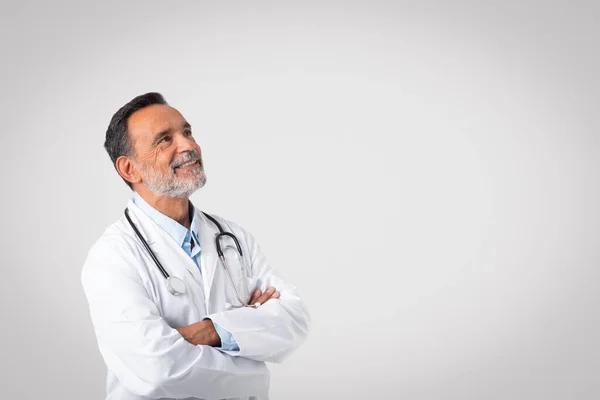 白いコートに身を包んだ自信に満ちた白人の成熟した医者は 灰色の背景 スタジオに隔離されたコピースペースを見ています アドバイス 生命保険 ヘルスケア オファー クリニックでの医療 — ストック写真