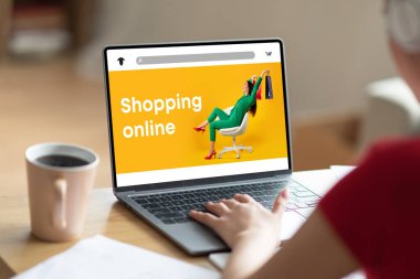 Kahve fincanı olan bir kadın masada oturuyor, ekranında moda mağazası olan bir laptop kullanıyor, evden yeni kıyafetler alıyor, online alışverişin ve boş zamanların tadını çıkarıyor, web sitesi, uygulama
