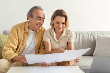 Mutlu Avrupalı üst düzey eşler dizüstü bilgisayarla faturaları ödüyor, kağıtları tutuyor ve internette bankacılık yapıyor, kanepeye oturuyor, boş yer açıyor.