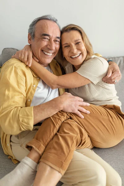 Excited Senior European Spouses Embracing Sitting Sofa Home Smiling Camera — Stock Photo, Image