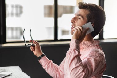 Pembe gömlekli çekici bir genç adam iş yerinde oturuyor, gözlük takıyor, telefonla konuşuyor, fotokopi odasına bakıyor. Girişimci iş ortağıyla konuştu