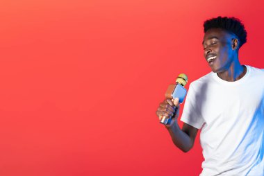 Karizmatik yetenekli, yakışıklı, beyaz tişörtlü genç adam kırmızı arka planda neon ışıkta şarkı söylüyor, Afrikalı Amerikalı adam karaoke yapıyor, gözleri kapalı, uzay boşluğunu kopyalıyor.