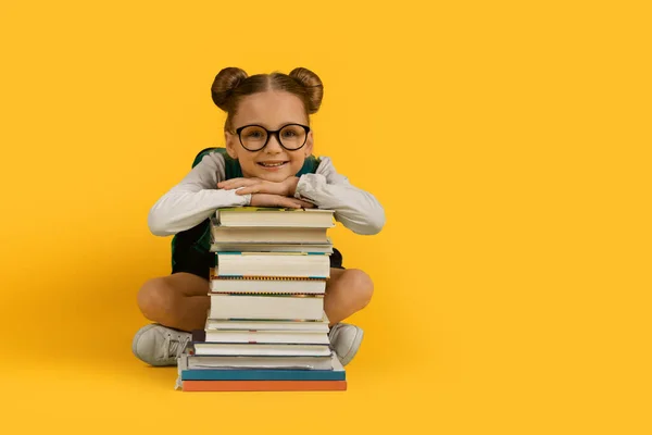 回到学校的概念 可爱的小女孩靠在书架上 微笑着拍照 眼镜中快乐的未成年女婴 在黄色的工作室背景上与人隔离 复制空间 — 图库照片