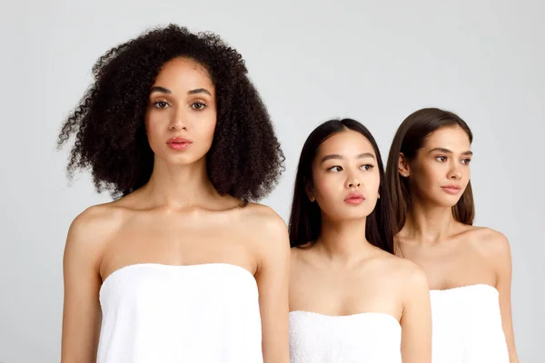 三个身穿白色浴巾的年轻多种族女子的画像 漂亮的卷曲黑人女子在镜头前 在灰色背景下合影 — 图库照片