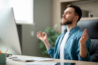 Zen kavramı. Ofiste meditasyon yapan sakin genç iş adamı, rahat erkek girişimci iş yerinde Zen Yogası yapıyor, son teslim tarihi stresiyle başa çıkıyor, masasında gözleri kapalı dinleniyor.
