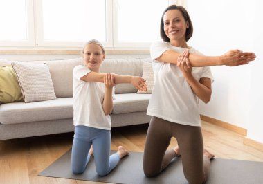 Mutlu bin yıllık beyaz kadın spor giyim ve genç kız yoga yapıyor, oturma odasının içinde el esneme egzersizi yapıyor. Aktif yaşam tarzı, evde spor, vücut bakımı.