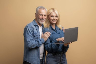 Beyaz saçlı yaşlı çift ve sarışın kadın bej arka planda modern bilgisayar kullanıyorlar, yeni ev arıyorlar, internetten mal ve hizmetlere para ödüyorlar. Yaşlılar için bilgisayar okuryazarlığı