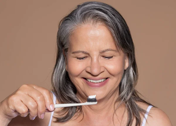 微笑的欧洲裔老年灰发女人用牙刷刷牙 享受日常生活 与米色工作室背景隔离 Higiena 牙科护理 — 图库照片