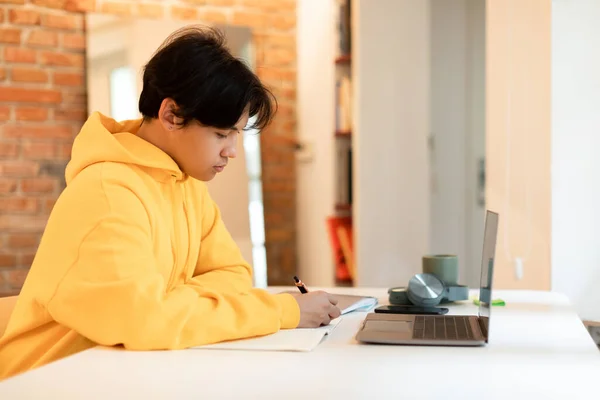 Eラーニング ラップトップで机に座って勉強している深刻な若いアジアの男は 自宅での彼の大学の宿題に焦点を当てノートを取り サイドビューショット インターネットと現代教育 — ストック写真