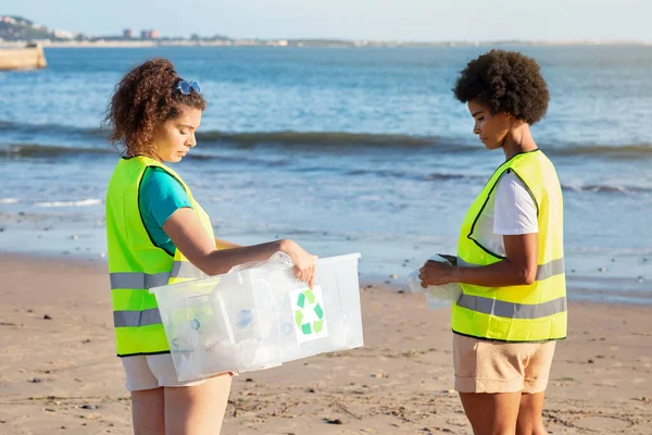 严重的青少年不同的女孩和女志愿者穿着背心在海滩收集垃圾和瓶子 生态工作 塑料回收利用 帮助自然和团队合作 环境保护 — 图库照片