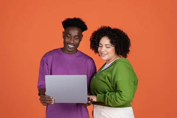 stock image Cheerful happy beautiful mixed race lovers african american guy and hispanic woman plus size using laptop on orange background, paying for goods and services on Internet