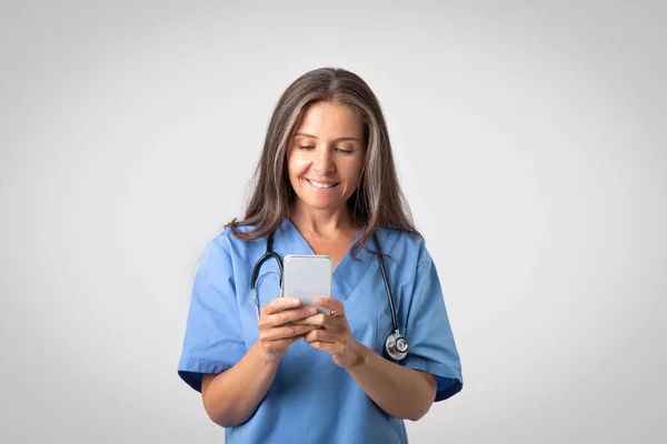 Professional Senior Female Physician Using Smartphone Medical App Standing Light — Stock Photo, Image