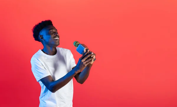 エンターテイメントと近代的な技術 幸せな感情的なハンサムな若い黒男の歌手保持マイク アフリカの男はネオンライトで赤の背景で実行 コピースペースとパノラマ — ストック写真