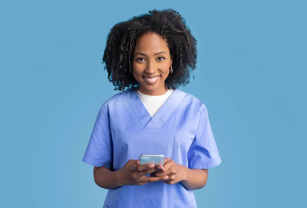 Positiva Joven Afroamericana Rizada Enfermera Uniforme Azul Mecanografía Charlando Teléfono —  Fotos de Stock