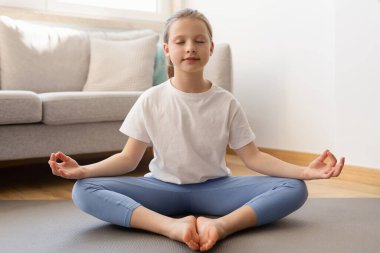 Spor giyim kuşamında, ciddi bir genç beyaz kız. Meditasyon yapıyor, yoga yapıyor. Oturma odasında tek başına rahatlıyor. Spor, spor, sağlık hizmetleri