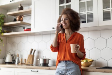 Neşeli siyah kadın, kahve içiyor ve cep telefonuyla konuşuyor, genç Afro-Amerikan bayan bardağı sıcak içecek ve keyifli cep telefonu sohbeti, bedava uzay...