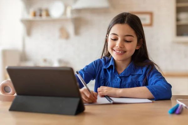 电子学习休闲活动 微笑着在数字平板电脑学习的初中生女孩 在家里做在线学习笔记 虚拟教室的女学生坐在房间的课桌前 — 图库照片