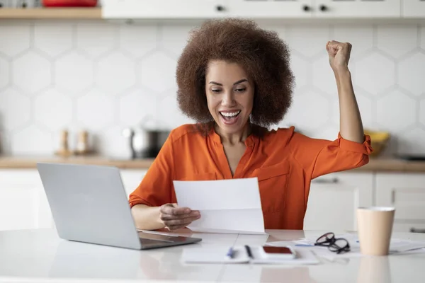 喜びに満ちた黒人女性の肖像 キッチンで手紙を読む ノートパソコンで机に座って メール文書をチェックします 衝撃的な拳と成功を祝う — ストック写真