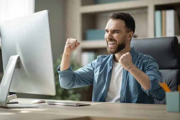 stock image Cheerful Young Businessman Looking At Computer Screen In Office And Celebrating Success, Joyful Excited Male Entrepreneur Shaking Fists And Shouting Yes, Emotionally Reacting To Good News