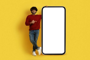 Çevrimiçi asistan, sohbet robotu, yapay zeka. Gülümseyen kıvırcık sakallı Hintli adam. Sıradan kıyafetli. Büyük cep telefonunu işaret ediyor.