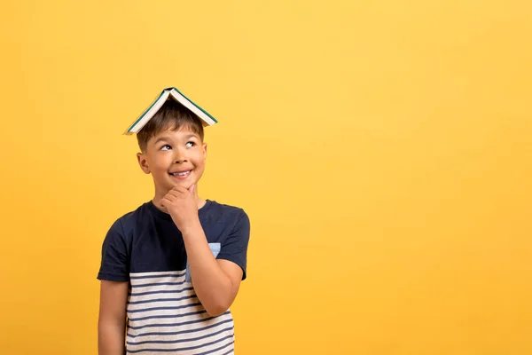 彼の頭の上に本が彼のあごに触れ 黄色の背景に隔離されたコピースペースを見てとカジュアル服で幸せなかわいいハンサムな白人の学校高齢者の少年 児童文学 — ストック写真