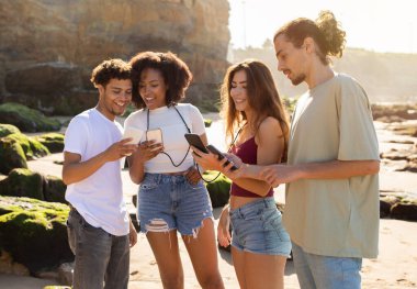 Binlerce yıllık neşeli uluslararası insanlar yaz tatilinin tadını çıkarıyorlar, eğleniyorlar, sahilde akıllı telefonlardan sohbet ediyorlar. Blog, sosyal ağ uygulaması, aktif yaşam tarzı, hafta sonu birlikte boş zaman.