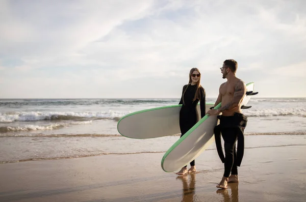 Młoda Para Surferów Spaceruje Deskami Surfingowymi Plaży Zachodzie Słońca Szczęśliwi — Zdjęcie stockowe