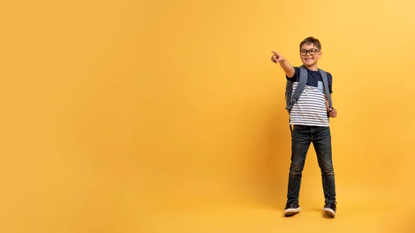 儿童教育 可爱而快乐的高加索男孩学生 戴着眼镜 背包指向广告和微笑的复制空间 隔离在黄色的背景下 — 图库照片